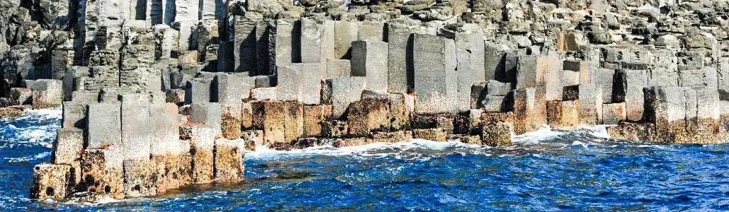 Hexagonal columnar lava cliffs rising vertically from the sea, viewed from a railed boardwalk